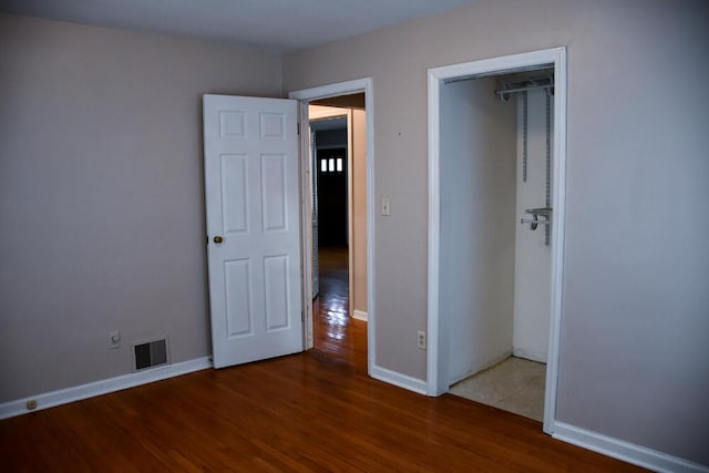 unfurnished bedroom featuring a closet, wood finished floors, visible vents, and baseboards