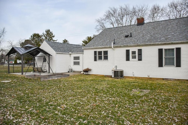 back of house with a shingled roof, a lawn, a chimney, a patio area, and central AC