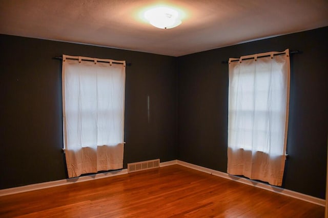 empty room with visible vents, baseboards, and wood finished floors