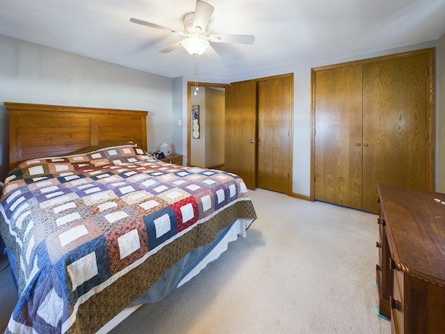 bedroom featuring ceiling fan, light carpet, and multiple closets