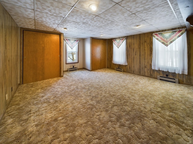 carpeted spare room with baseboard heating and wood walls