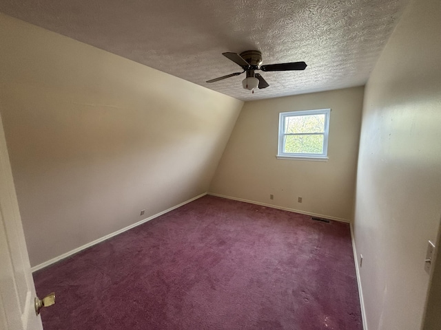 additional living space featuring a textured ceiling, baseboards, visible vents, ceiling fan, and carpet floors