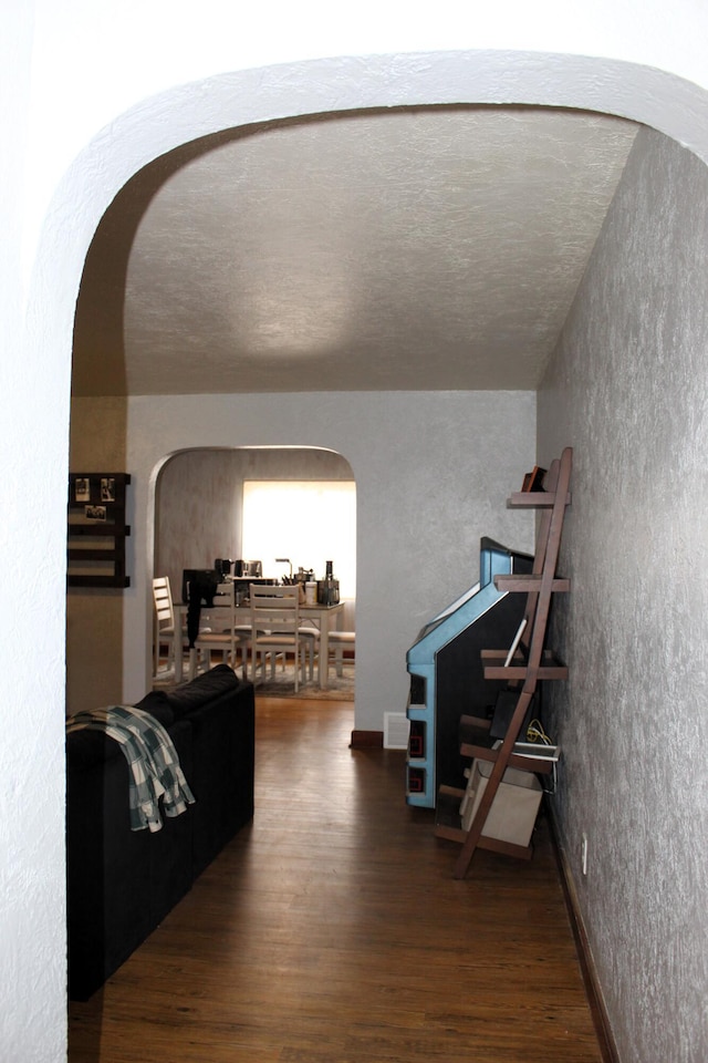 living area featuring arched walkways, a textured wall, and wood finished floors