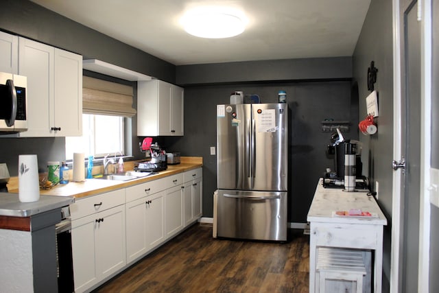 kitchen featuring stainless steel appliances, a sink, white cabinets, light countertops, and dark wood-style floors