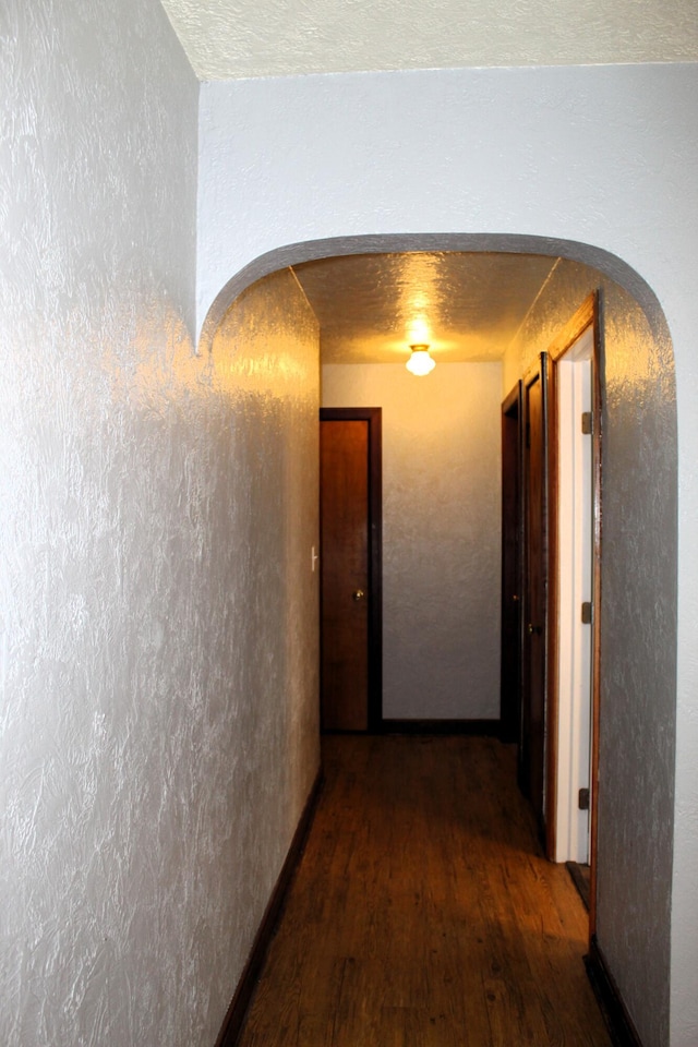 hall featuring a textured ceiling, arched walkways, wood finished floors, and a textured wall