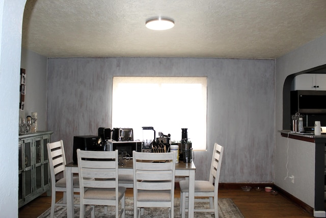 dining room featuring arched walkways, wood finished floors, and baseboards