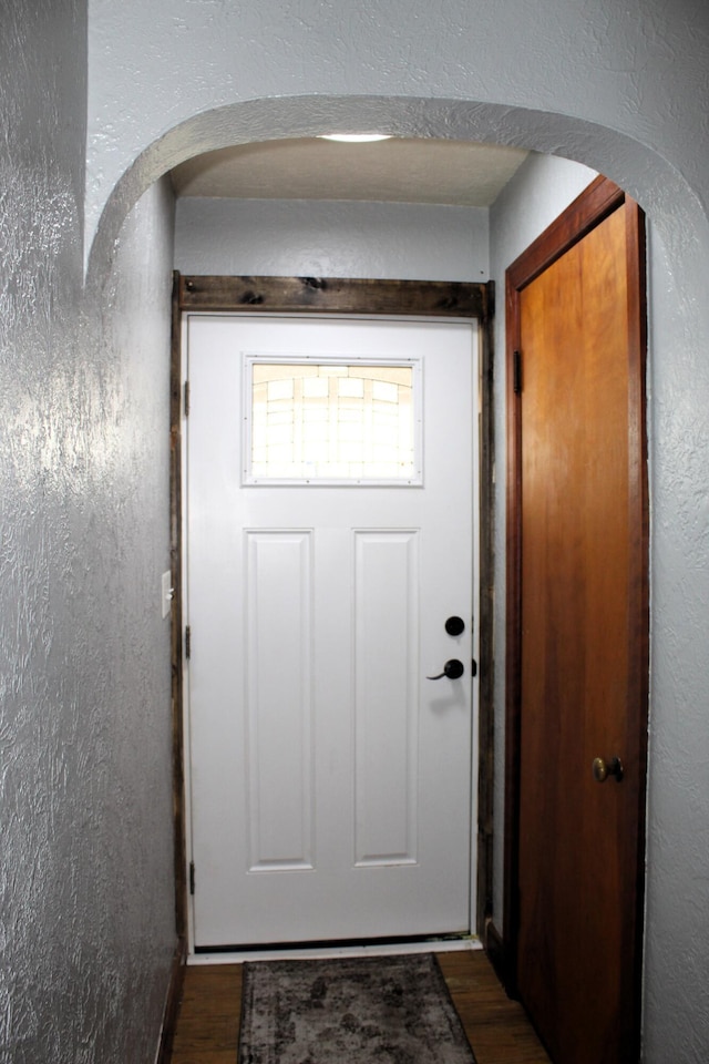 entryway featuring dark wood-style floors, arched walkways, and a textured wall