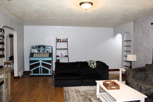 living area with built in features, arched walkways, dark wood-style flooring, and a textured ceiling