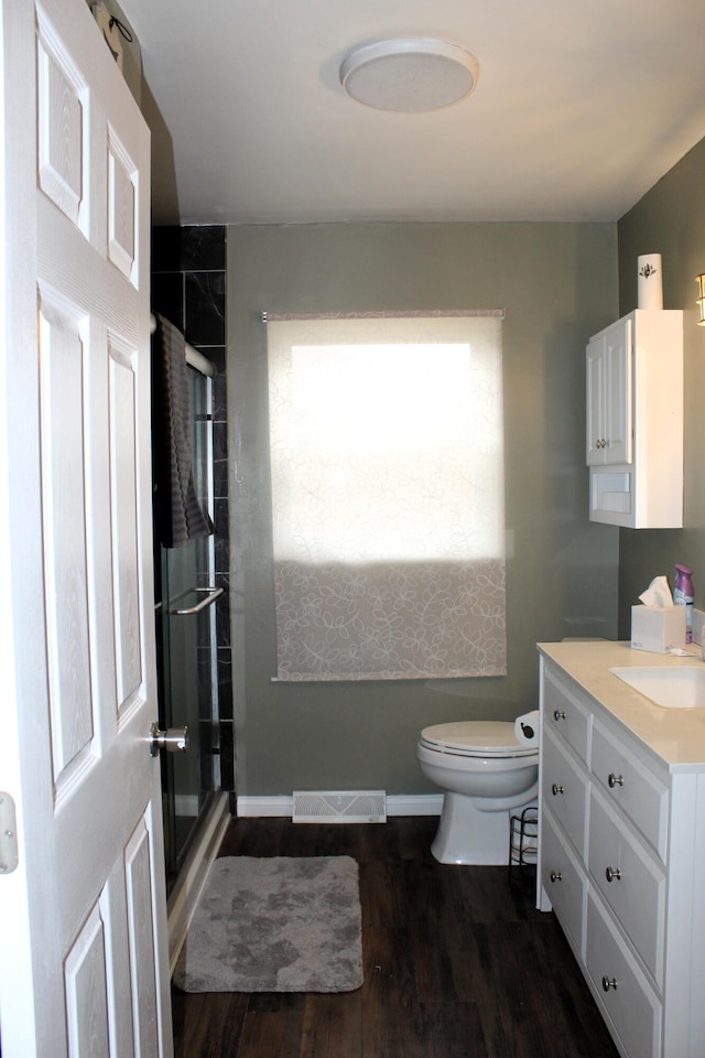 bathroom with visible vents, toilet, vanity, a shower stall, and wood finished floors