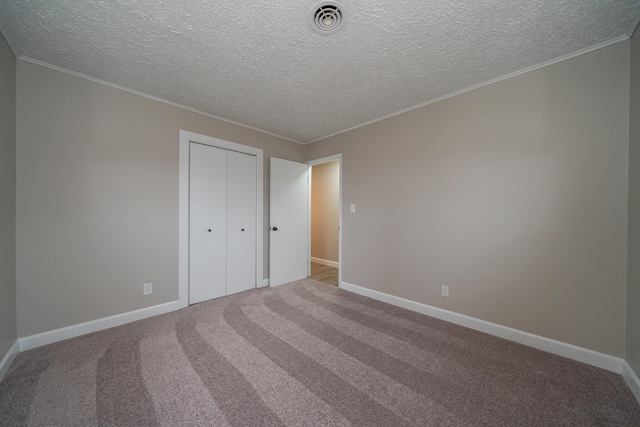 unfurnished bedroom featuring light colored carpet, ornamental molding, a closet, and a textured ceiling