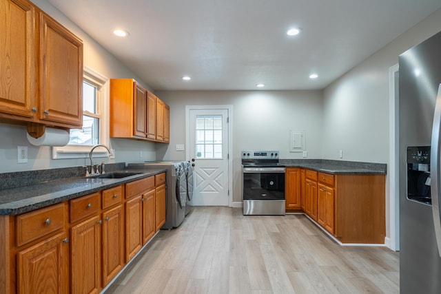 kitchen featuring sink, light hardwood / wood-style flooring, appliances with stainless steel finishes, dark stone countertops, and independent washer and dryer