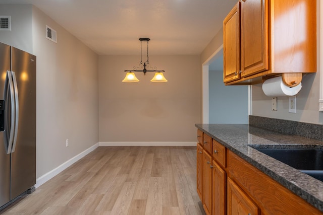 kitchen with pendant lighting, dark stone counters, stainless steel fridge, and light wood-type flooring