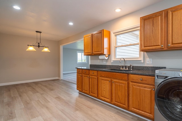 kitchen with sink, hanging light fixtures, washer / clothes dryer, dark stone counters, and light wood-type flooring