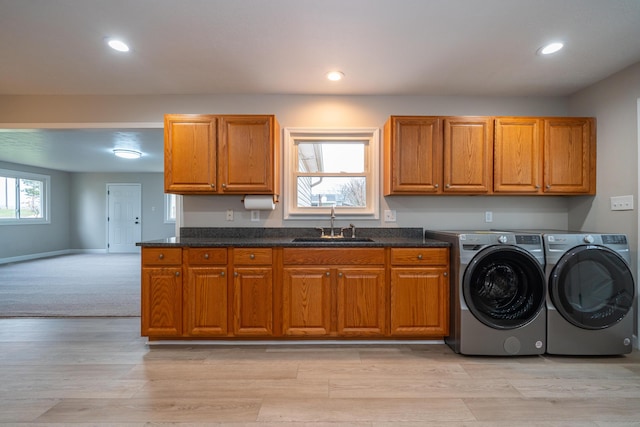 interior space featuring washing machine and clothes dryer, dark stone counters, sink, and light wood-type flooring