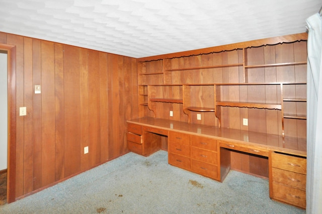 unfurnished office featuring carpet flooring, wood walls, and built in desk