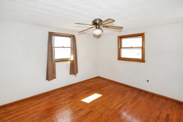 spare room with a wealth of natural light, ceiling fan, baseboards, and wood-type flooring