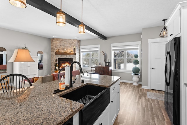 kitchen featuring dark stone counters, freestanding refrigerator, white cabinetry, and a sink