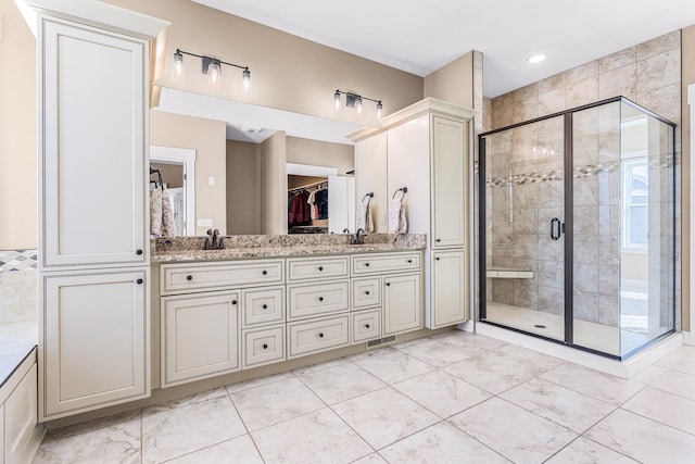 bathroom with double vanity, a shower stall, a walk in closet, and a sink