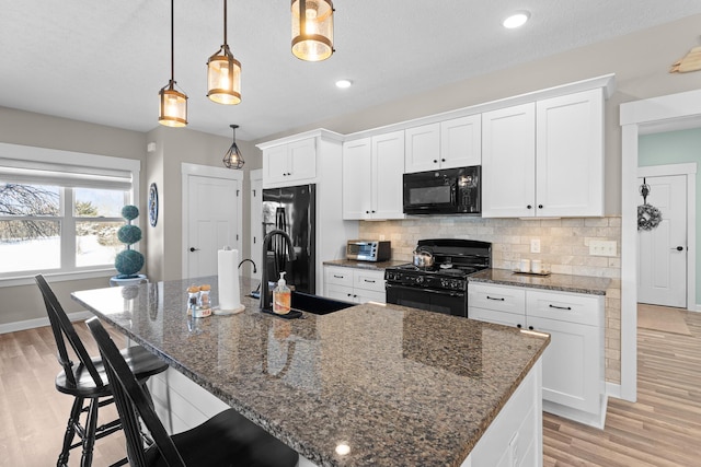 kitchen with a center island with sink, dark stone counters, white cabinets, decorative light fixtures, and black appliances