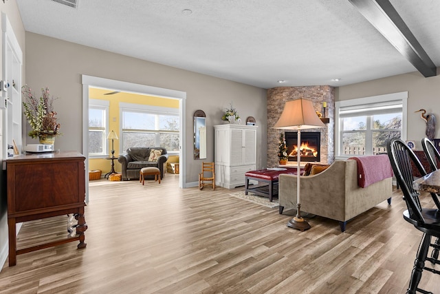 living area with a textured ceiling, a stone fireplace, a wealth of natural light, and light wood-style flooring