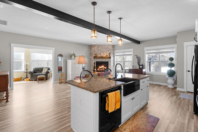 kitchen with open floor plan, white cabinets, an island with sink, dark stone counters, and black appliances