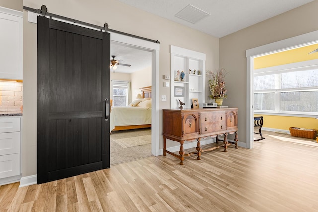 interior space with light wood finished floors, a barn door, visible vents, and baseboards