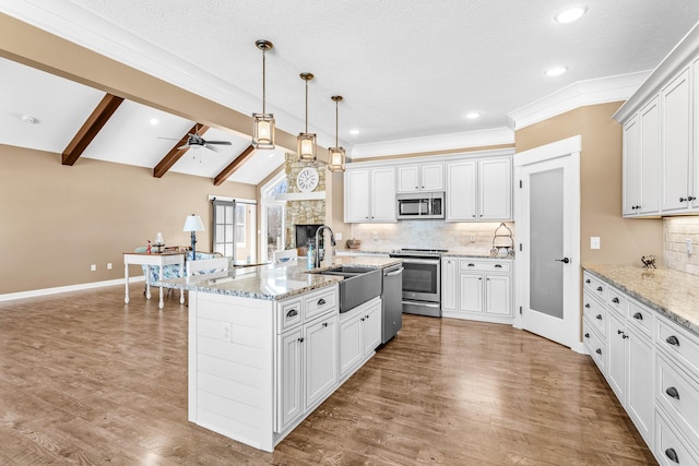 kitchen with lofted ceiling with beams, a sink, white cabinets, appliances with stainless steel finishes, and a center island with sink