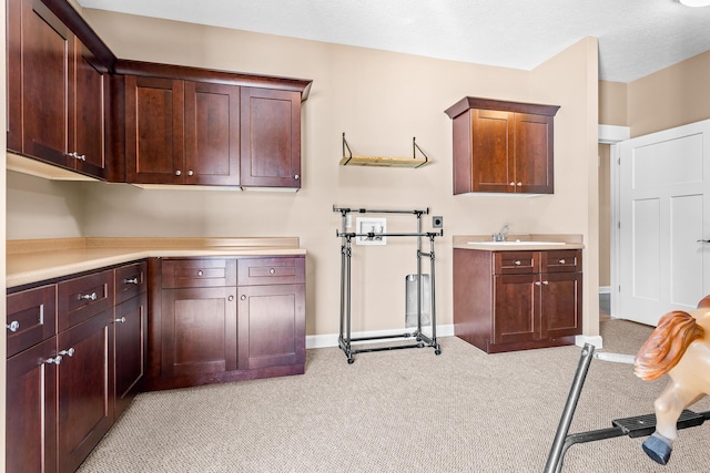 kitchen featuring baseboards, light countertops, a sink, and light colored carpet