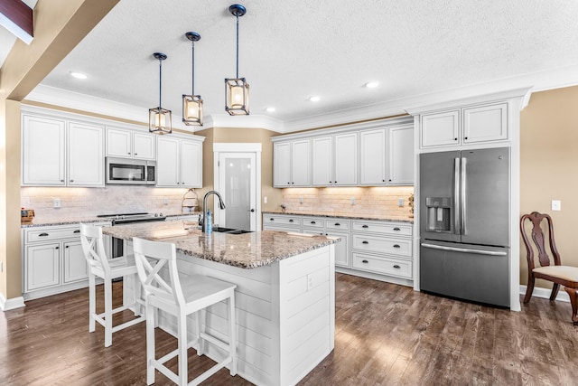 kitchen with a center island with sink, appliances with stainless steel finishes, white cabinets, a sink, and light stone countertops