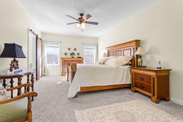 bedroom with a barn door, a ceiling fan, light carpet, a textured ceiling, and baseboards