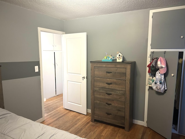 bedroom with baseboards, a textured ceiling, and wood finished floors