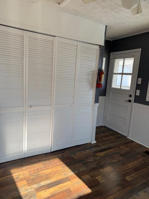 foyer entrance with dark wood-style floors, a textured ceiling, a ceiling fan, and a wainscoted wall