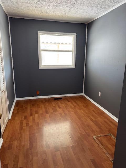 spare room featuring visible vents, ornamental molding, a textured ceiling, wood finished floors, and baseboards