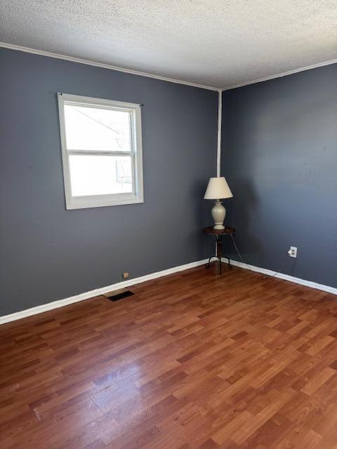 spare room with baseboards, visible vents, ornamental molding, and dark wood-style flooring