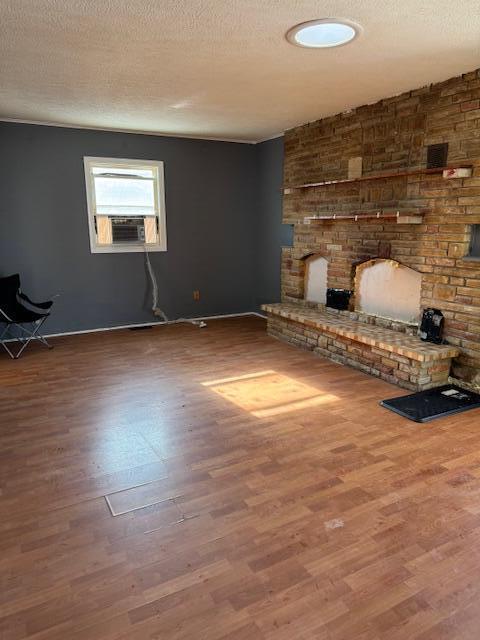 interior space with a large fireplace, a textured ceiling, cooling unit, and wood finished floors