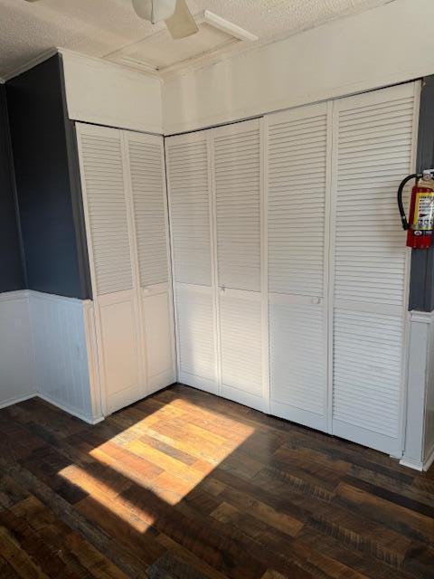 unfurnished bedroom featuring a ceiling fan, wainscoting, dark wood-style flooring, a textured ceiling, and a closet