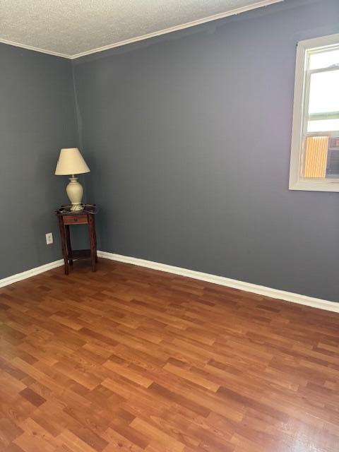 spare room featuring a textured ceiling, ornamental molding, wood finished floors, and baseboards