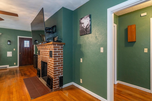 living area with visible vents, a textured wall, a brick fireplace, wood finished floors, and baseboards