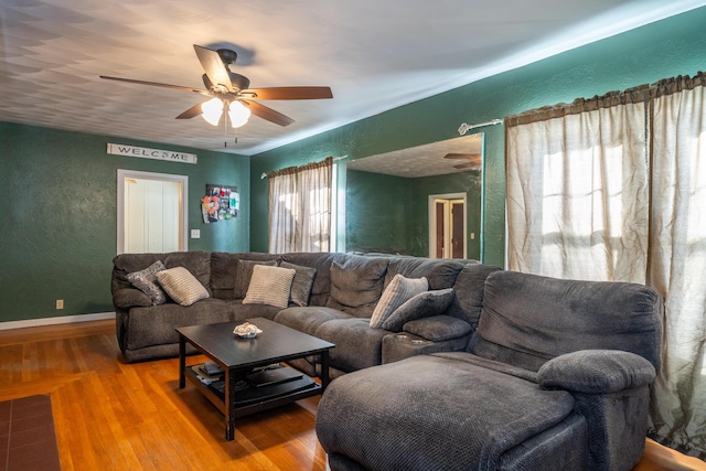 living area featuring ceiling fan, a textured wall, wood finished floors, and baseboards