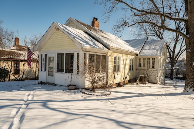 snow covered rear of property with a sunroom and a chimney