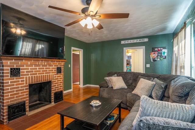 living room featuring baseboards, visible vents, ceiling fan, wood finished floors, and a brick fireplace