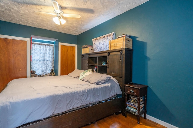 bedroom with a textured ceiling, wood finished floors, two closets, and baseboards