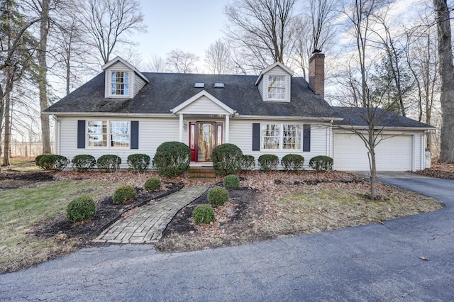 cape cod-style house featuring aphalt driveway, a chimney, an attached garage, and a shingled roof