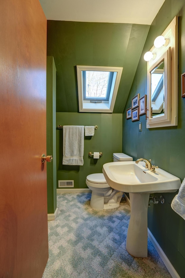 half bathroom featuring vaulted ceiling with skylight, toilet, baseboards, and visible vents