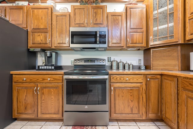4602 State Route 273, Belle Center, OH 43310 - kitchen featuring stainless steel appliances, light tile patterned floors, brown cabinets, glass insert cabinets, and light countertops