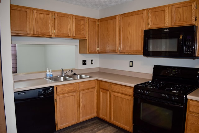 kitchen with dark wood finished floors, light countertops, a textured ceiling, black appliances, and a sink