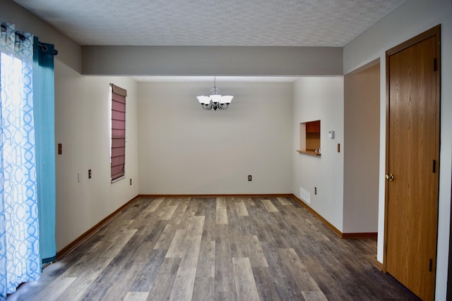 unfurnished dining area featuring a textured ceiling, wood finished floors, visible vents, and an inviting chandelier