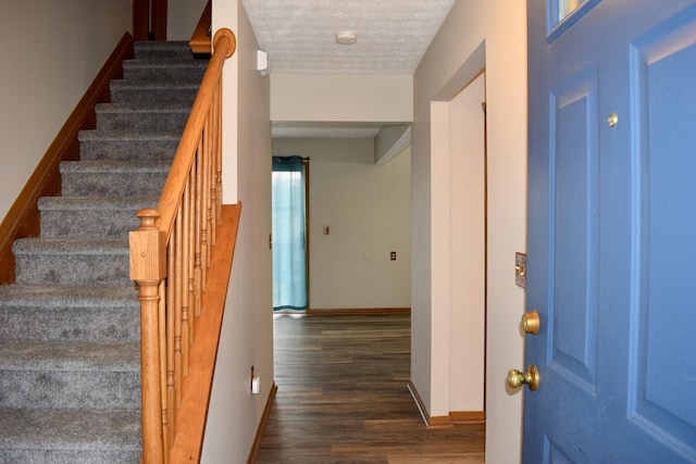 entrance foyer featuring a textured ceiling, stairway, dark wood finished floors, and baseboards