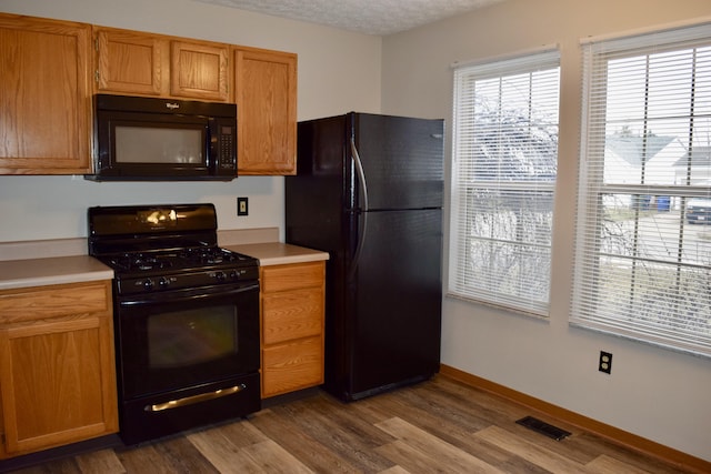 kitchen featuring wood finished floors, visible vents, light countertops, brown cabinets, and black appliances