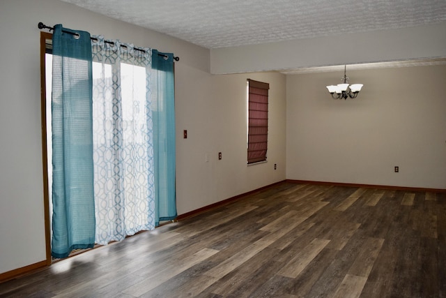 spare room featuring a chandelier, dark wood-style flooring, a textured ceiling, and baseboards